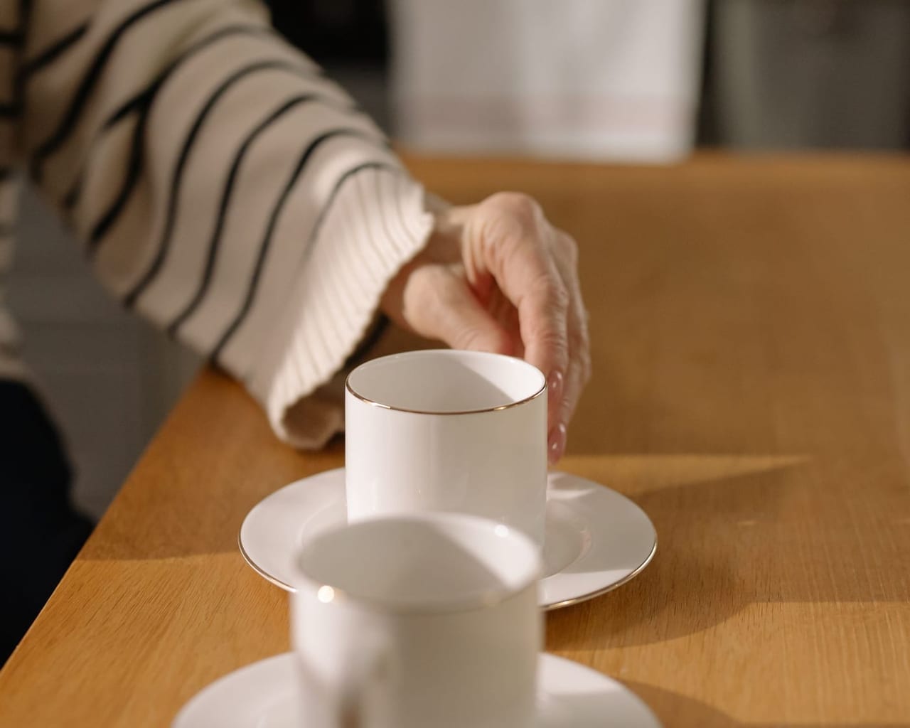 Eine Hand greift an einem Holztisch nach einer Tasse