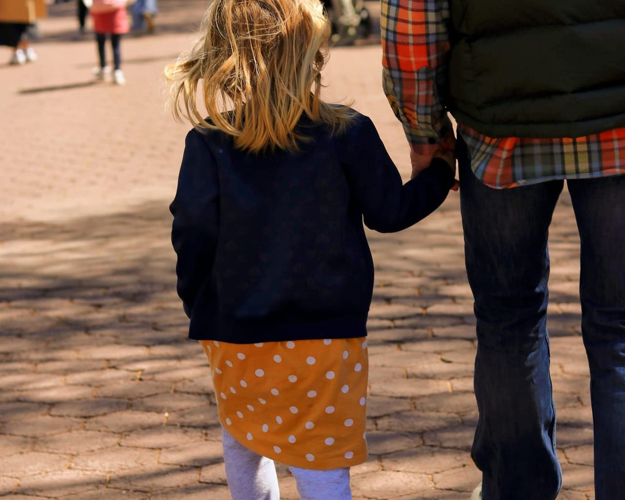 Ein Kind geht, von hinten gesehen, an der Hand eines Erwachsenen einen Weg entlang